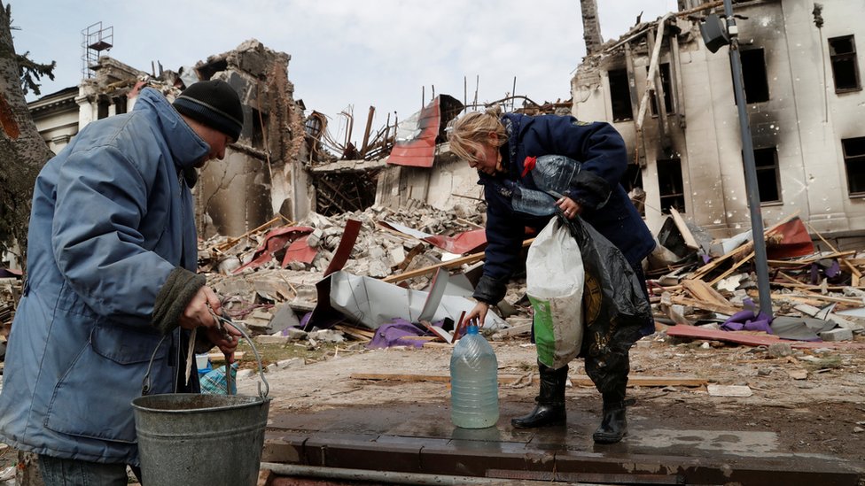 Local residents draw water from a well near the building of a destroyed theatre in Mariupol