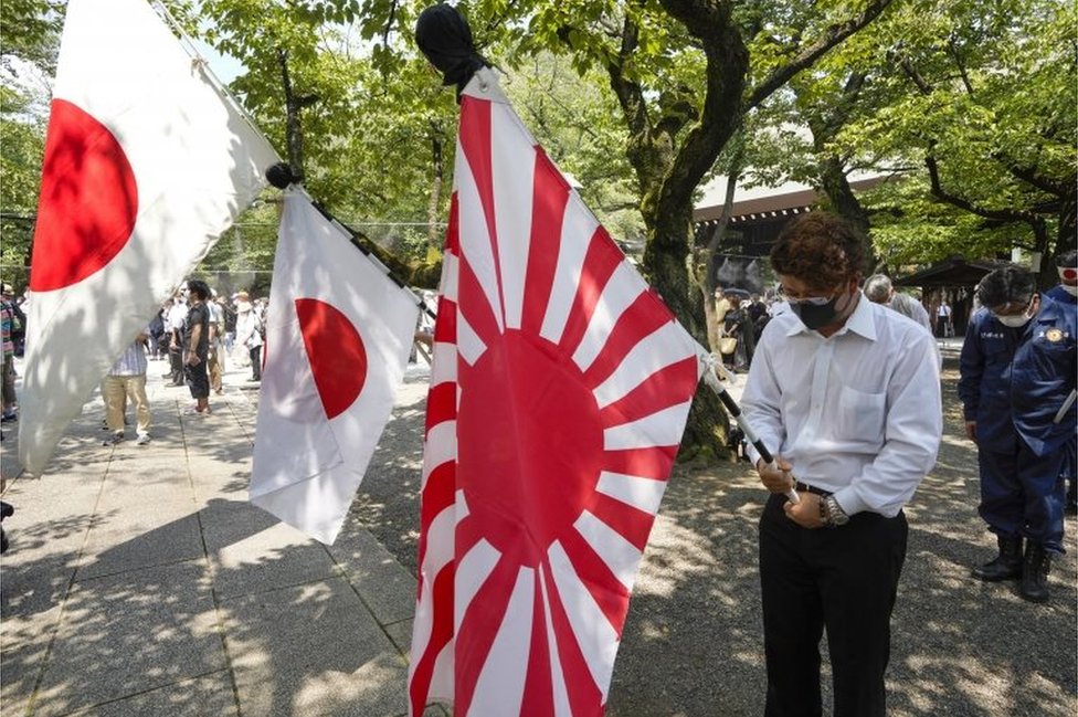 People holding Japan"s national flags and the rising sun flag offer one minute silence for the war dead at Yasukuni Shrine