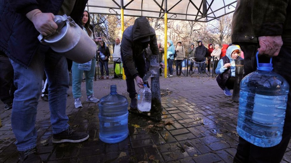 Грурра людей с пластиковыми бутылками набирает воду из колонки