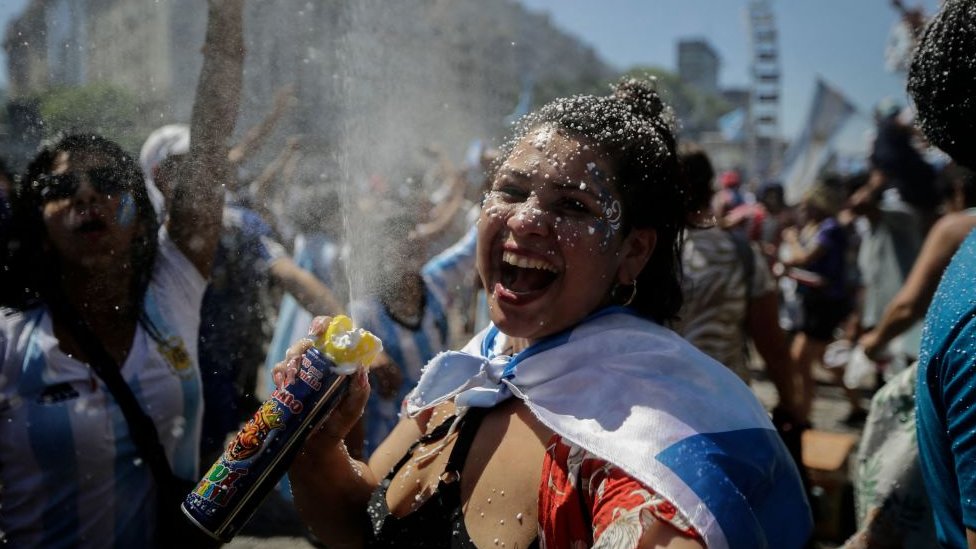 Mujer celebra con un spray de espuma y vestida con la bandera de Argentina.