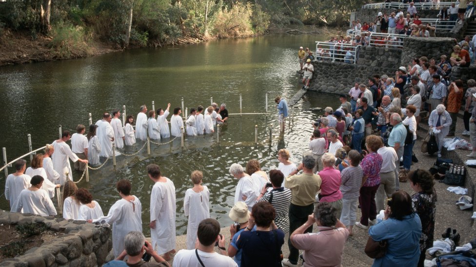 Группа людей в белых рубахах стоят в воде реки