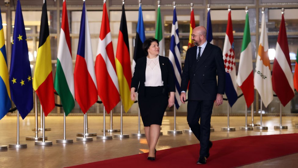 Мужчина и женщина идут по красной ковровой дорожке вдоль флагов стран ЕС
