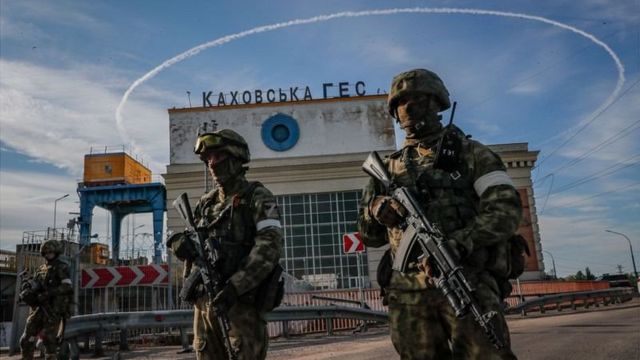 Двое солдат с автоматами на фоне бетонного здания, на котором написано Каховская ГЭС