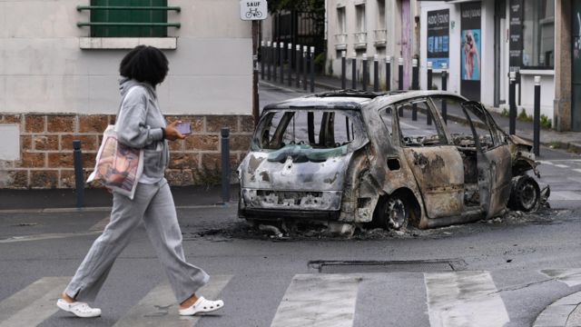 Женщина идет мимо сгоревшей машины