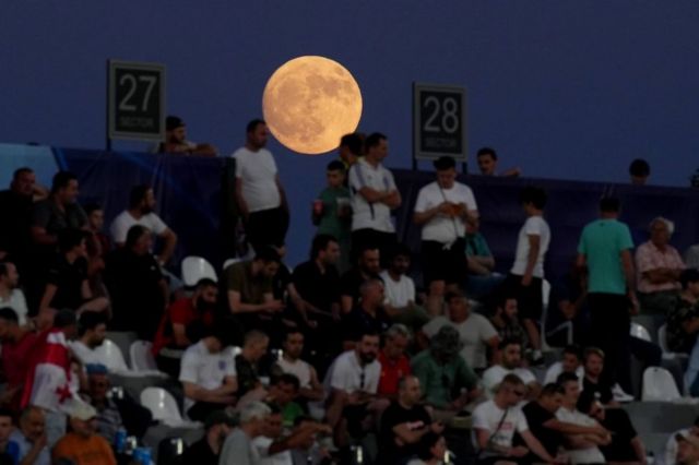 Зрители, наблюдающие за спортивным матчем, не замечают позади себя полную луну в Кутаиси, Грузия