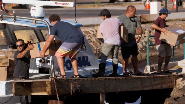 Люди загружают коробки с гуманитарной помощью в лодку