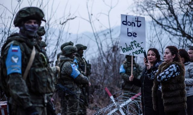 Женщины с плакатом "Не будьте безучастны" стоят перед российскими миротворцами