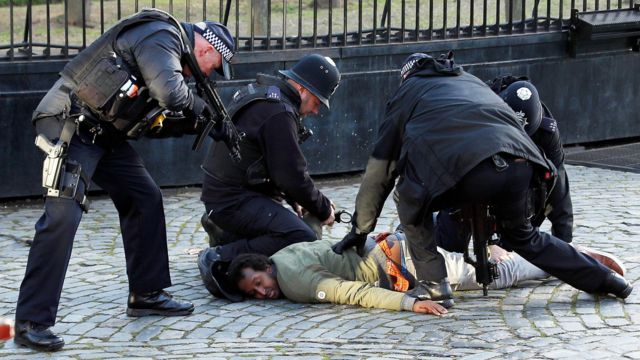 Двое вооруженных полицейских помогают двум постовым задерживать человека, пытавшегося прорваться в здание британского парламента