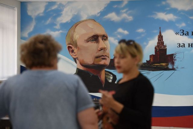 Люди на фоне плаката с изображением Путина