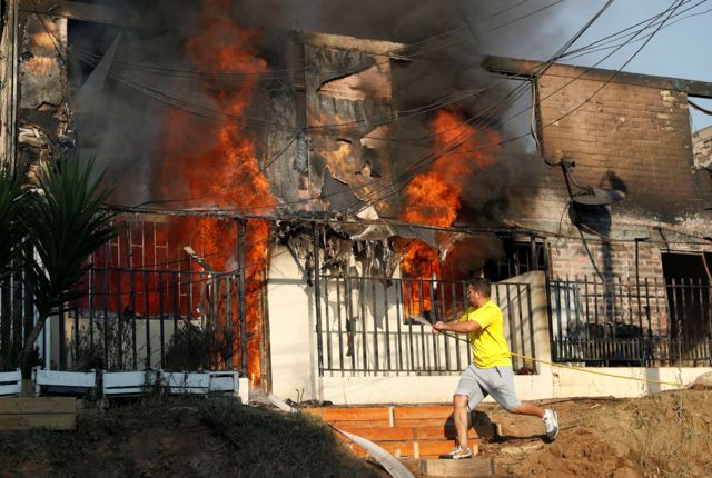 Человек с шлангом рядом с горящим домом