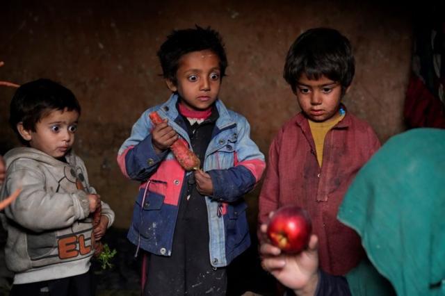 Афганские дети смотрят на яблоко, которое их мать принесла домой после того, как просила милостыню в лагере для беженцев на окраине Кабула