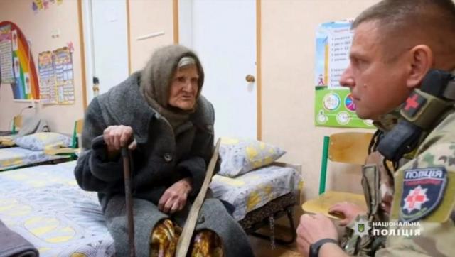 Пожилая женщина на кровати разговаривает с мужчиной в форме